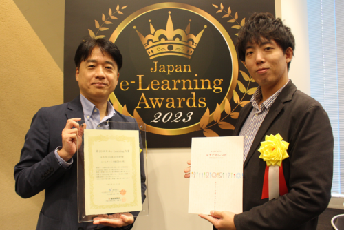 日本e-Learning大賞のロゴ前で記念撮影を撮るエームアカデミー担当者